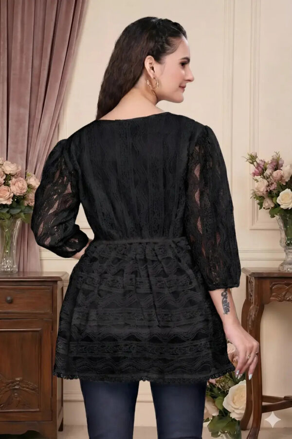 Woman wearing a black lace dress in an elegant room with floral arrangements.