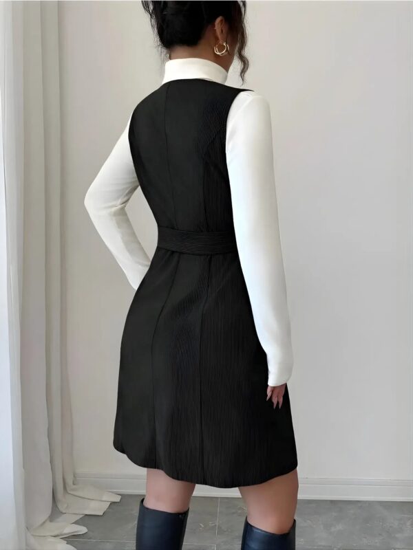 Person wearing a black pinafore dress over a white shirt against a neutral background