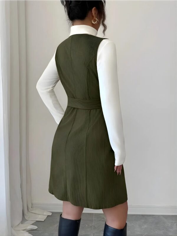 Person wearing a green dress over a white shirt against a plain background
