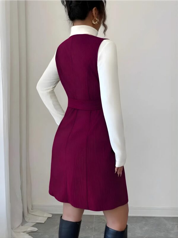 Person wearing a white long-sleeve shirt and a purple dress against a plain background
